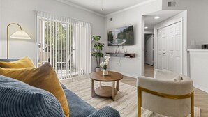 Una sala de estar con un sofá, una mesa de centro, una silla, un televisor y una puerta que da a otra habitación.
