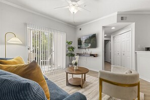 Uma sala de estar com sofá, mesa de centro, poltrona, televisão e uma porta que dá para outro cômodo.
