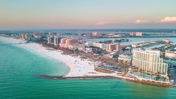 Vista aérea de una ciudad costera con playa, hoteles y puerto deportivo.
