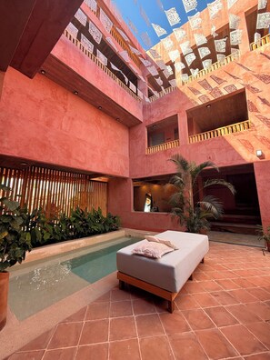 Un atrium à plusieurs niveaux doté d’une piscine, d’un espace détente avec un canapé et offrant une vue sur le ciel à travers des motifs ajourés sur les murs.