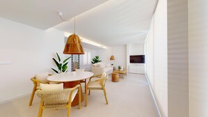 A modern living room with a round dining table, wicker chairs, a sofa, and a TV mounted on the wall. - 501 Mirasol eme by Maison El Ático (Arenales Del Sol, Los)