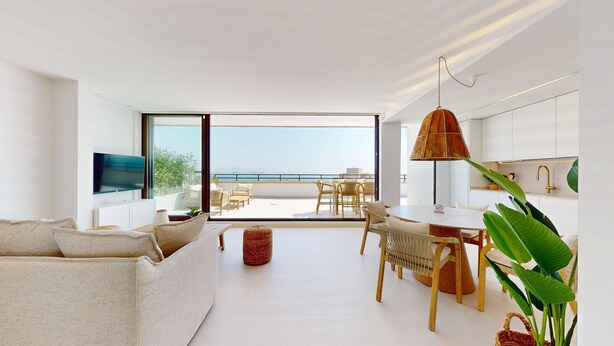 A modern living room with a large window overlooking a balcony with a view of the sea. There is a dining area with a round table and chairs, and a kitchen area with a large window and a hanging lamp. - 501 Mirasol eme by Maison El Ático (Arenales Del Sol, Los)