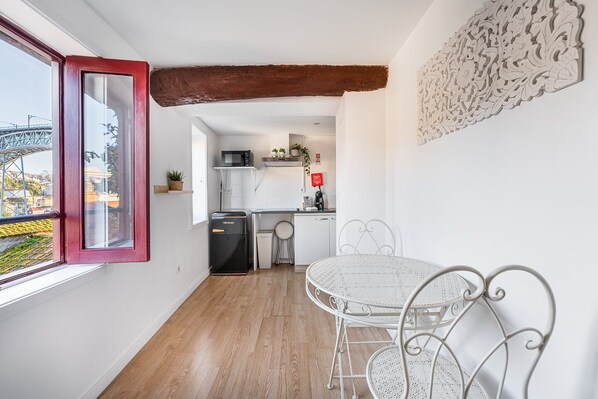 A compact kitchen with white cabinets, a microwave, and a coffee machine. There's a dining table with white chairs and a decorative wall piece.