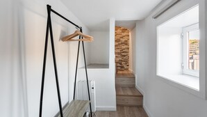 Un pasillo con un radiador, un banco de madera, un perchero de madera y una pared de piedra.