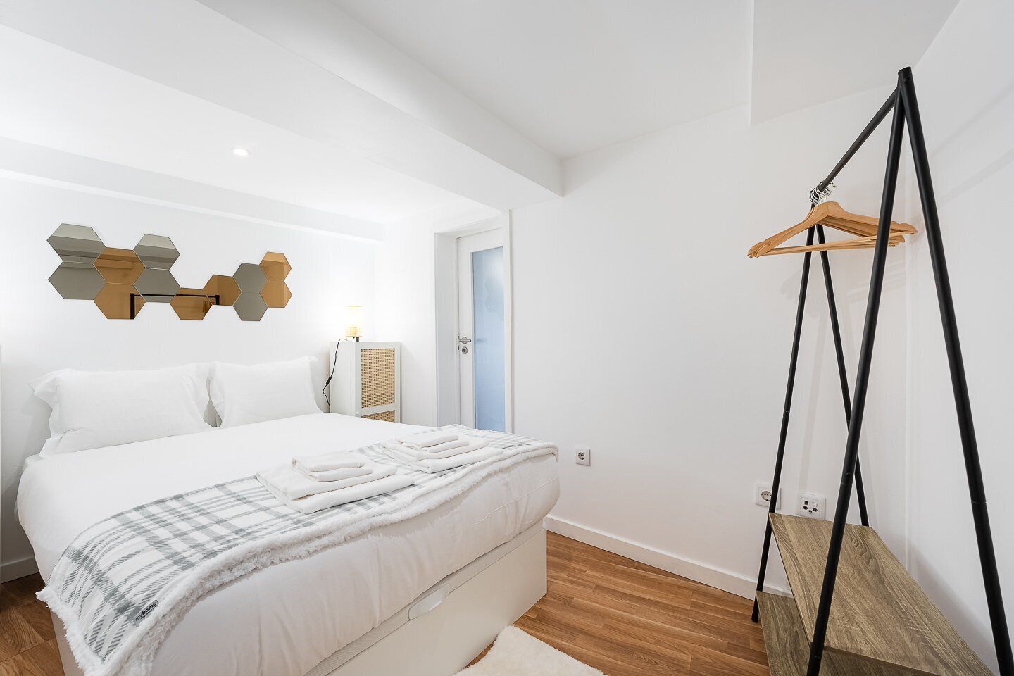 Une chambre moderne avec un grand lit, une table de chevet avec une lampe, un plancher en bois et un porte-manteau fixé au mur.