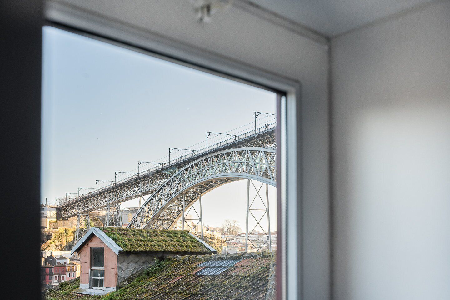 Blick auf eine Metallbrücke mit einer gewölbten Bögen, ein kleines rosafarbenes Gebäude mit einem grünen Dach und ein Fensterrahmen.