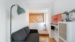 Una sala moderna con un sofá gris, una lámpara de pie, un televisor y bustos decorativos.