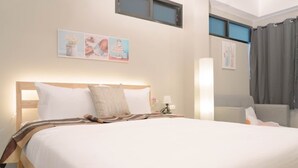Habitación de hotel con una cama grande, una mesita de noche con lámpara, una ventana y un cuadro en la pared.