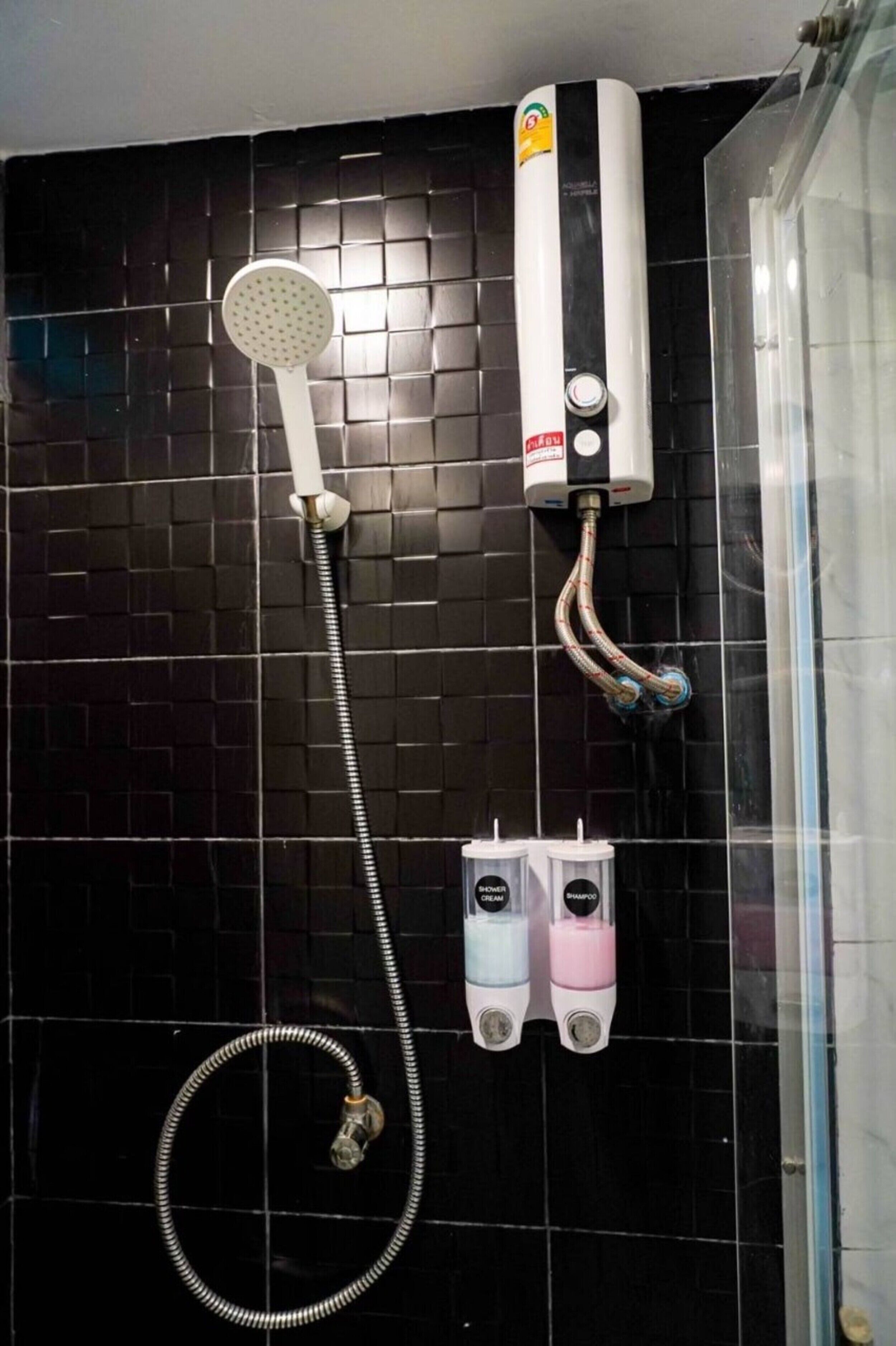 Ein Duschbereich mit Handbrause, Durchlauferhitzer an der Wand und zwei Seifenspendern.