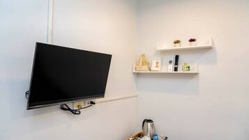 Habitación con televisor montado, cafetera, botella de agua y dos estantes con objetos decorativos.