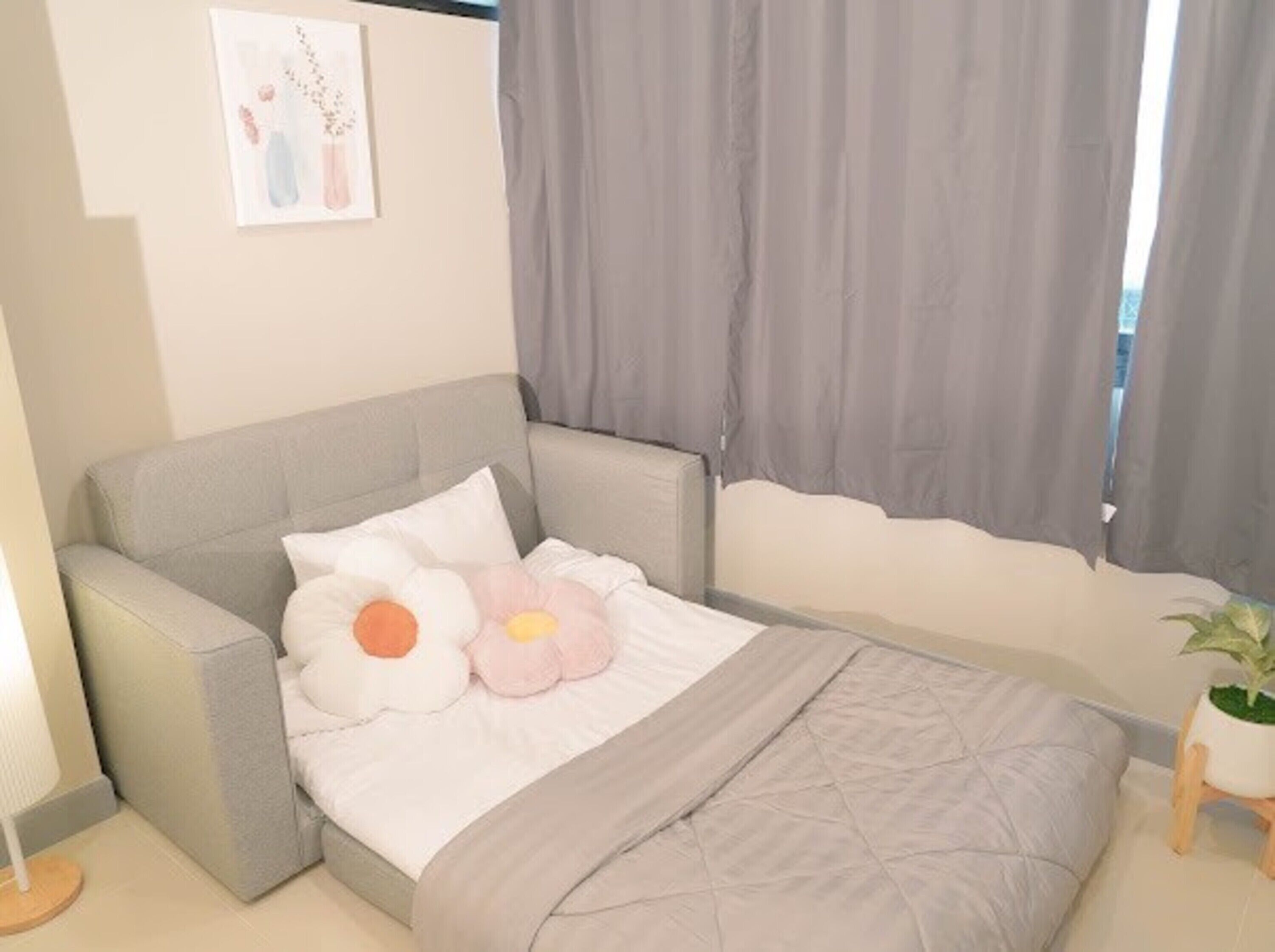 A bedroom with a bed, two pillows, a bedside table, a lamp, and a window with curtains.