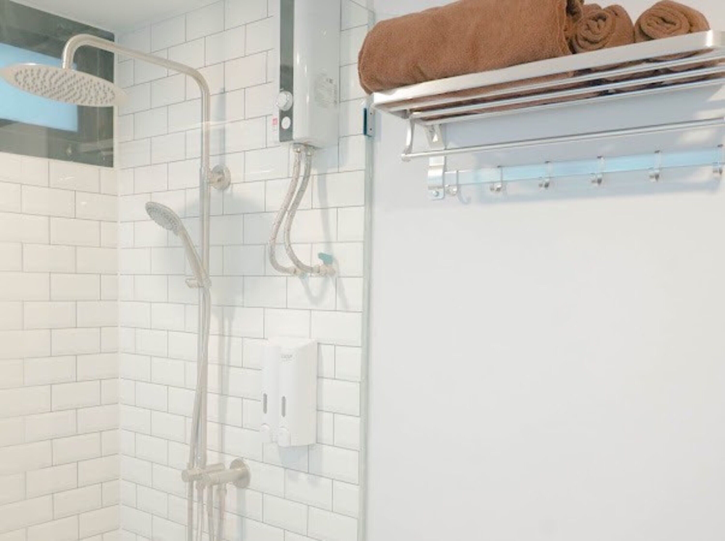 A shower with a handheld showerhead, a wall-mounted faucet, and a towel rack with towels.