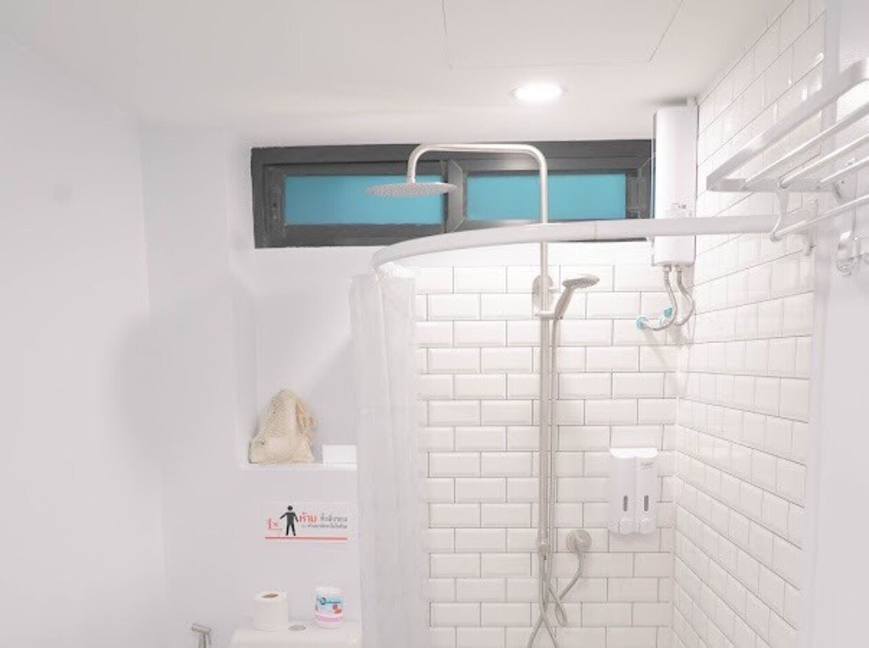 A modern bathroom with white tiled walls, a shower area, and a small shelf with toiletries.