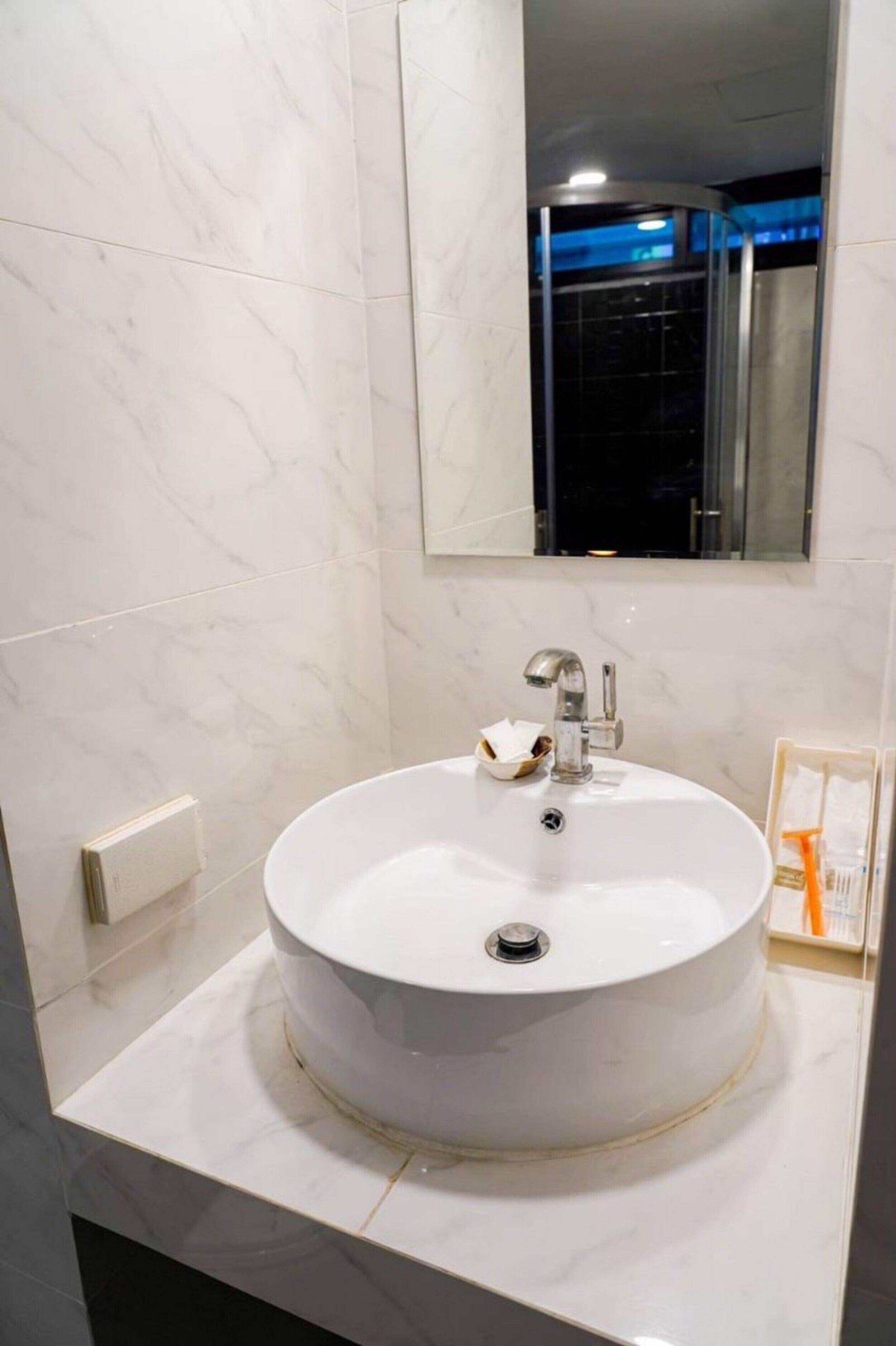 A bathroom with a round white sink, a mirror above it, and a framed picture on the wall.
