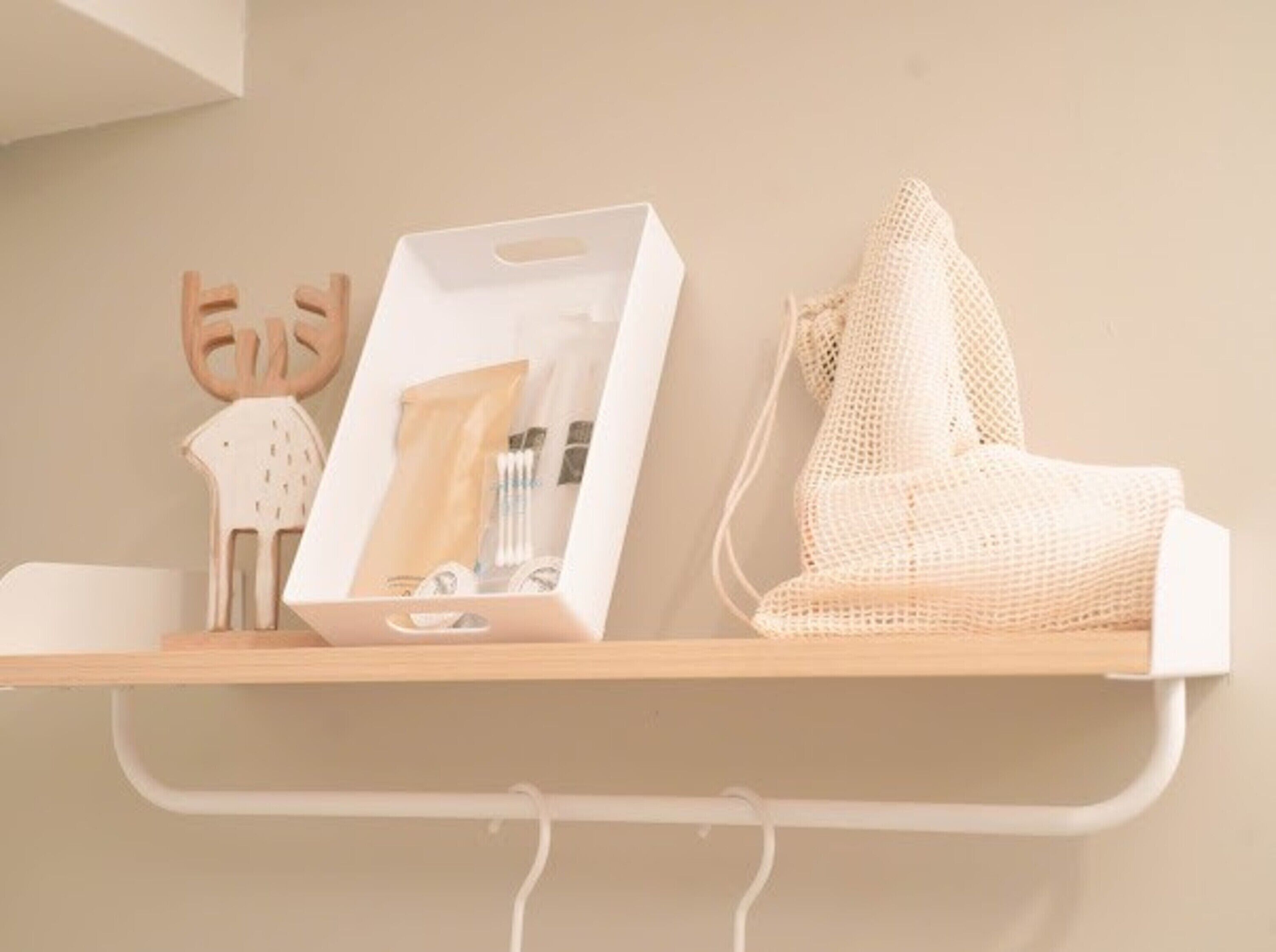 A shelf with a white box containing toiletries, a woven bag, and a wooden reindeer figure.