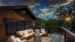 A wooden deck with wicker furniture, a stone fire pit, and a view of the sunset. - Beautiful 4-bedroom close to Sequoia Nat’l Park w/ WiFi, Pool, Spa, Pet Friendly (Three Rivers)