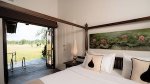 A bedroom with a bed, pillows, a nightstand, a lamp, and a painting of lotus flowers.