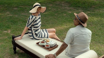 A couple sitting on a bed with a tray of tea and a teapot.
