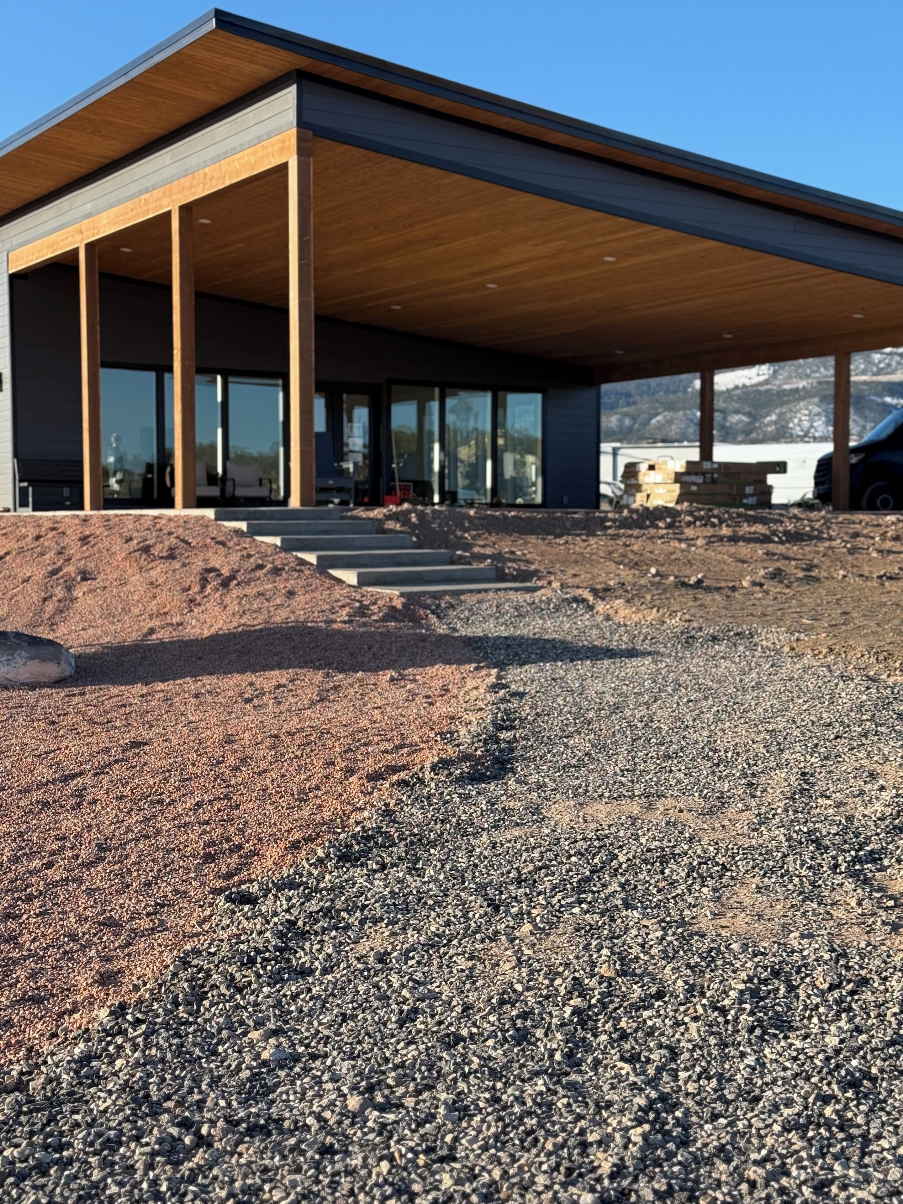 A modern building with a covered outdoor area, large windows, and a gravel ground.