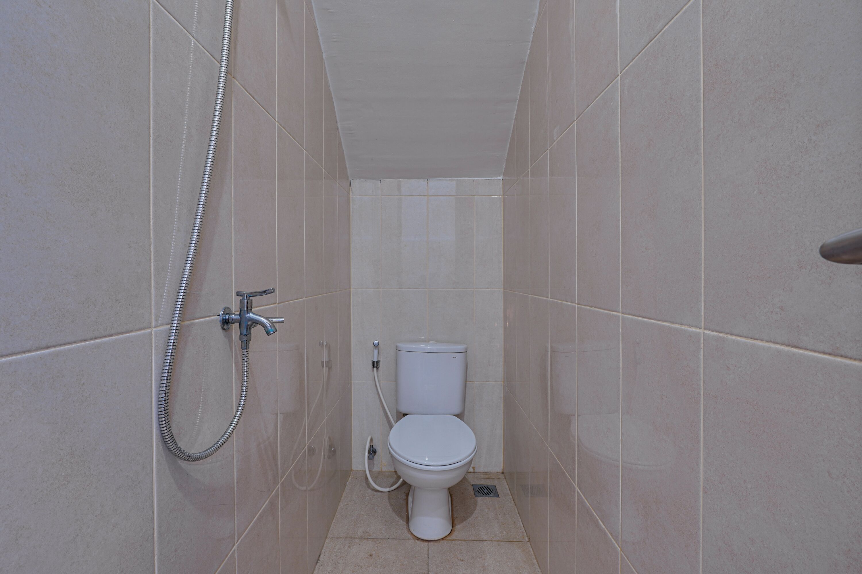 A small, tiled bathroom with a toilet, a shower, and a toilet paper holder.