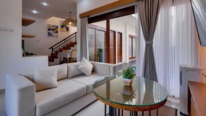 A modern living room with a sofa, a glass coffee table, and a staircase leading to other rooms. - Villa Boswelia Seminyak (Seminyak)