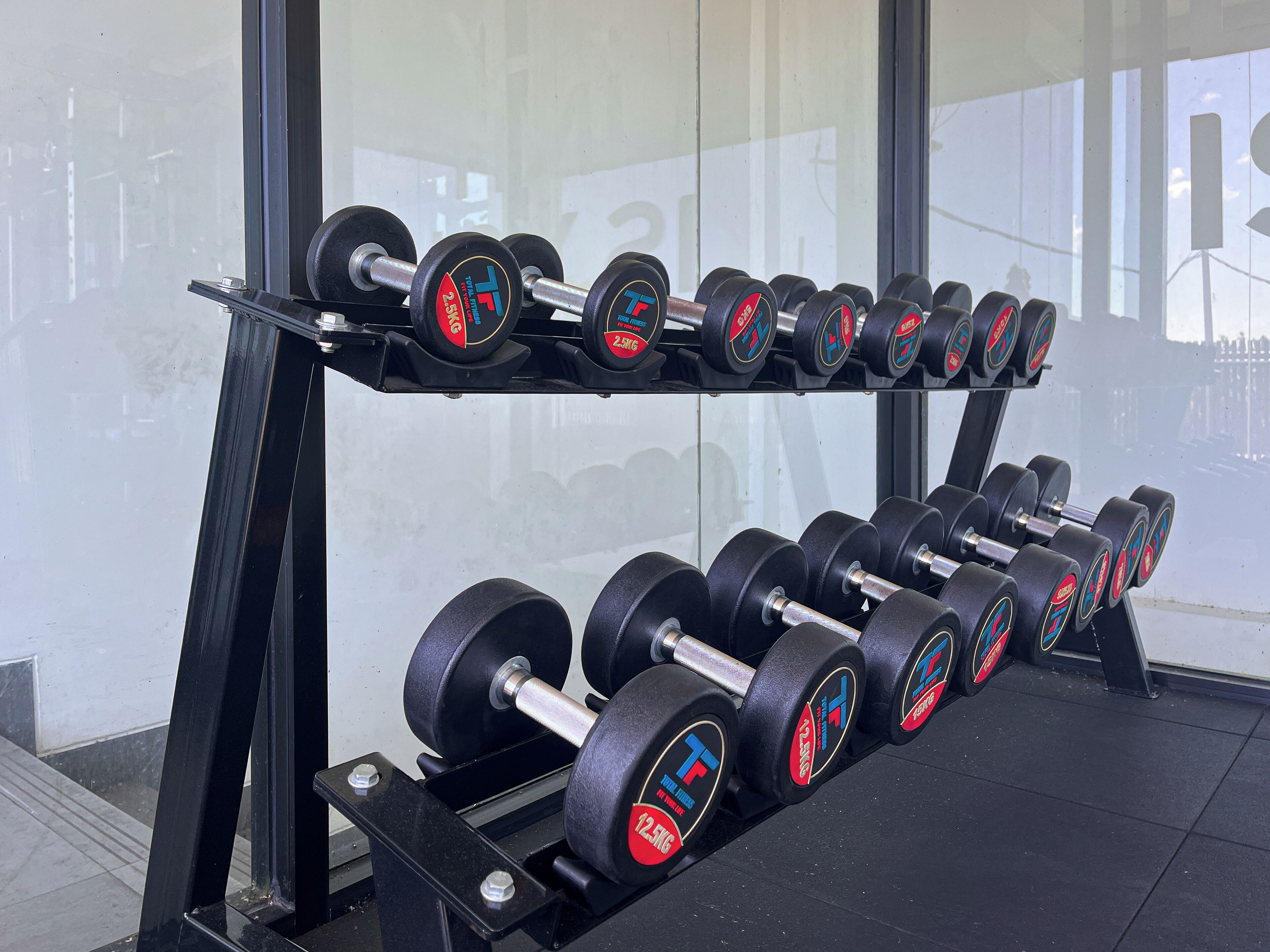 A rack of dumbbells with weight markings, positioned in a gym with a large window in the background.
