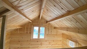 Un dormitorio de ático con techo inclinado y una ventana pequeña con vidrios formando un patrón de rombos.