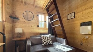 Una habitación tipo cabaña acogedora, con sofá, escalera, ventana, lámpara y calefactor.