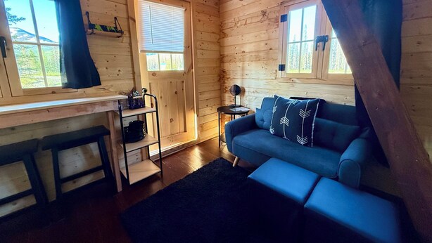 Interior acogedor de una cabaña con detalles de madera, un sofá, una mesita y una ventana con cortinas.
