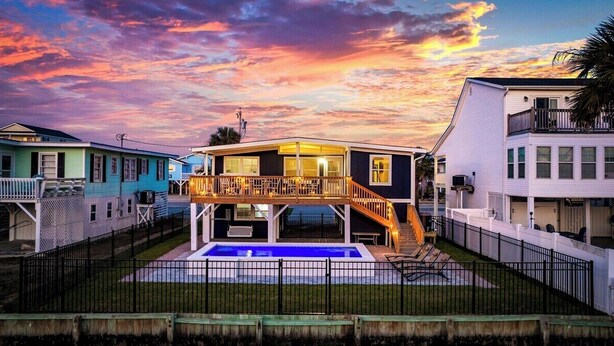 Una casa de dos pisos con balcón, piscina y patio cercado.