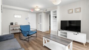 A modern living room with a flat-screen TV, a blue chair, a grey sofa, and a wooden coffee table. - Bay Harbor Sunset Apt 3B (Bay Harbor Islands)