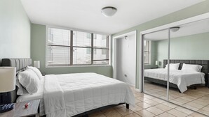 A modern bedroom with a bed, bedside table, lamp, and a large mirror. - Bay Harbor Sunset Apt 3B (Bay Harbor Islands)