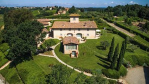 Eine große Villa mit einem zentralen Innenhof, umgeben von üppigen Gärten und einer hügeligen Landschaft.