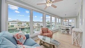 A spacious room with a large window overlooking a marina, a ceiling fan, and a dining area with white furniture.