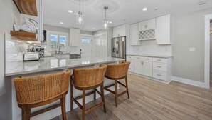A modern kitchen with white cabinets, a large island with bar stools, and a stainless steel refrigerator.