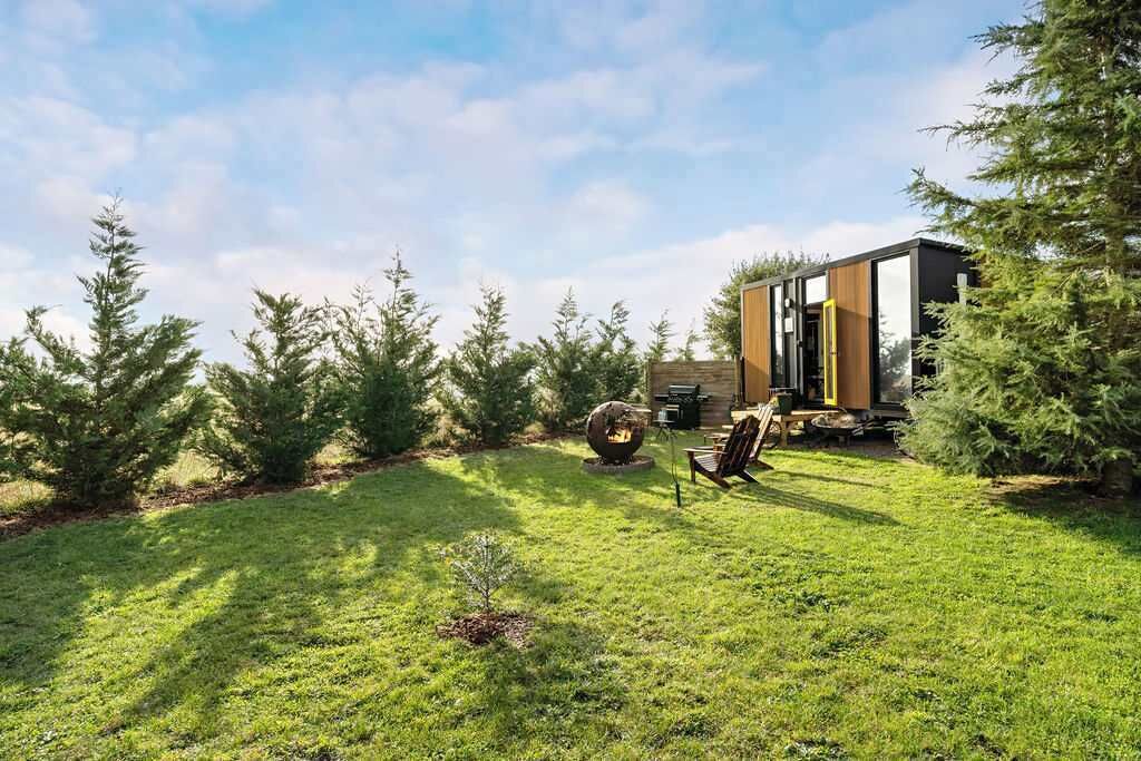 A modern house with a well-maintained lawn, outdoor seating, and a large tree in the foreground.
