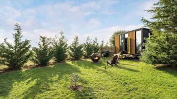 A modern house with a well-maintained lawn, outdoor seating, and a large tree in the foreground.