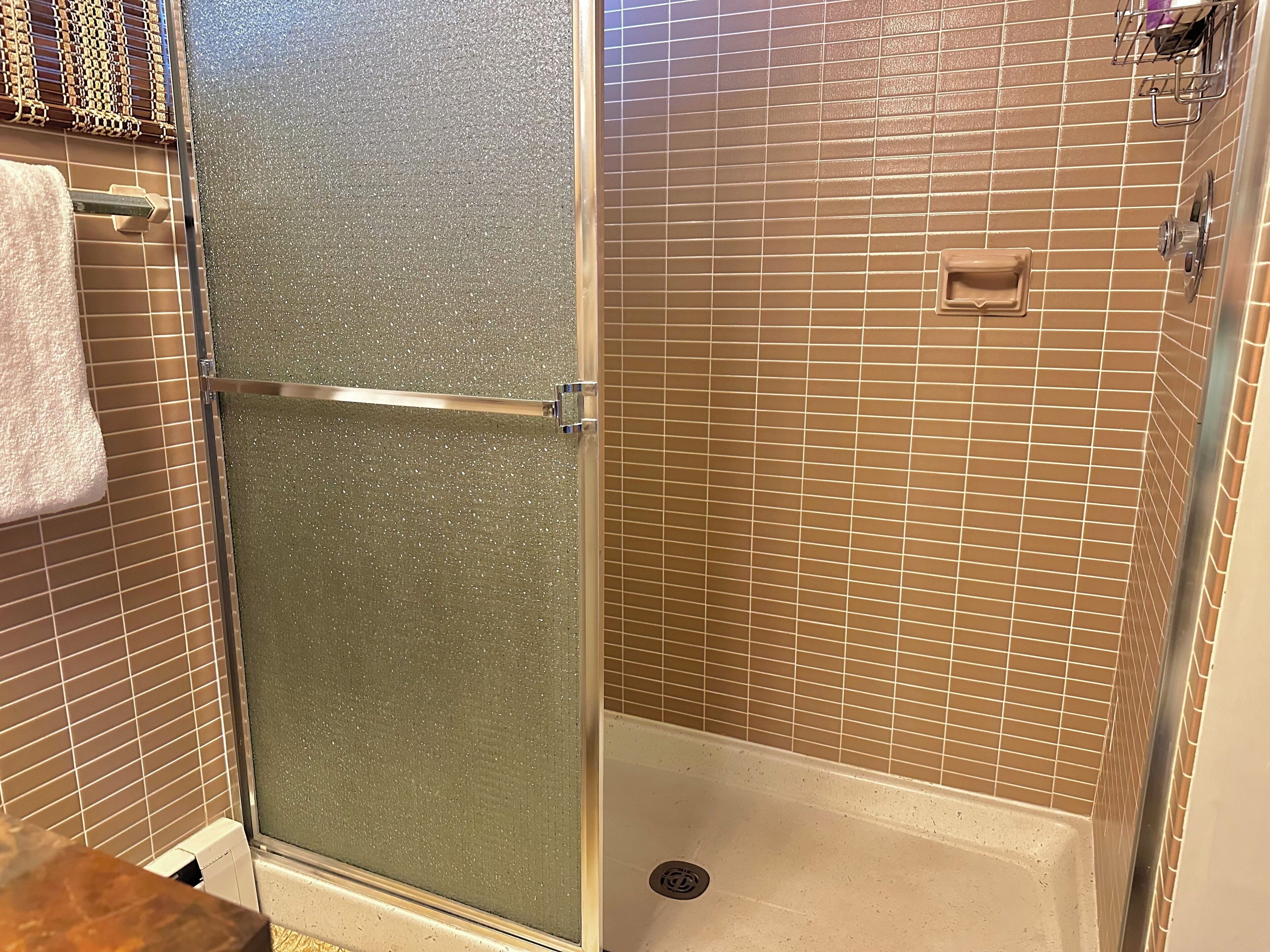 A shower with a glass door, tiled walls, and a towel rack.