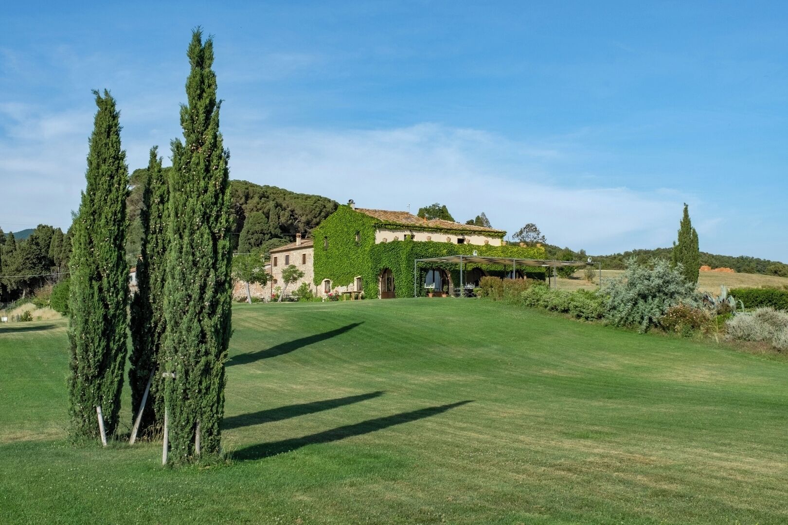 A large villa with a well-maintained lawn, a pergola, and tall cypress trees.
