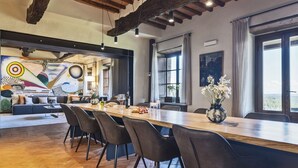 A modern dining area with a long wooden table, black chairs, and a view of the countryside through large windows.