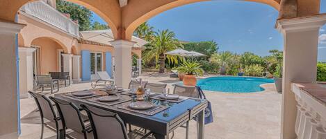 An outdoor dining area with a pool and palm trees.