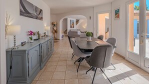 A modern kitchen with a dining area, featuring a long table with chairs, a built-in oven, and a large window providing a view of the outside.
