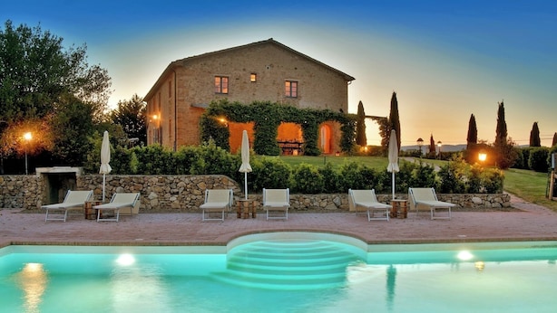 A pool area with lounge chairs and umbrellas, a stone wall, and a building with a stone facade and windows. - Villa Scuderie -  Guardistallo, Pisa (Guardistallo)
