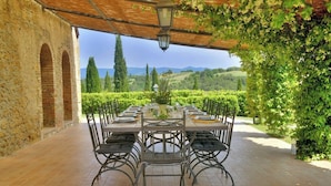 An outdoor dining area with a long table set for six, surrounded by brick walls and a pergola with climbing plants. - Villa Scuderie -  Guardistallo, Pisa (Guardistallo)