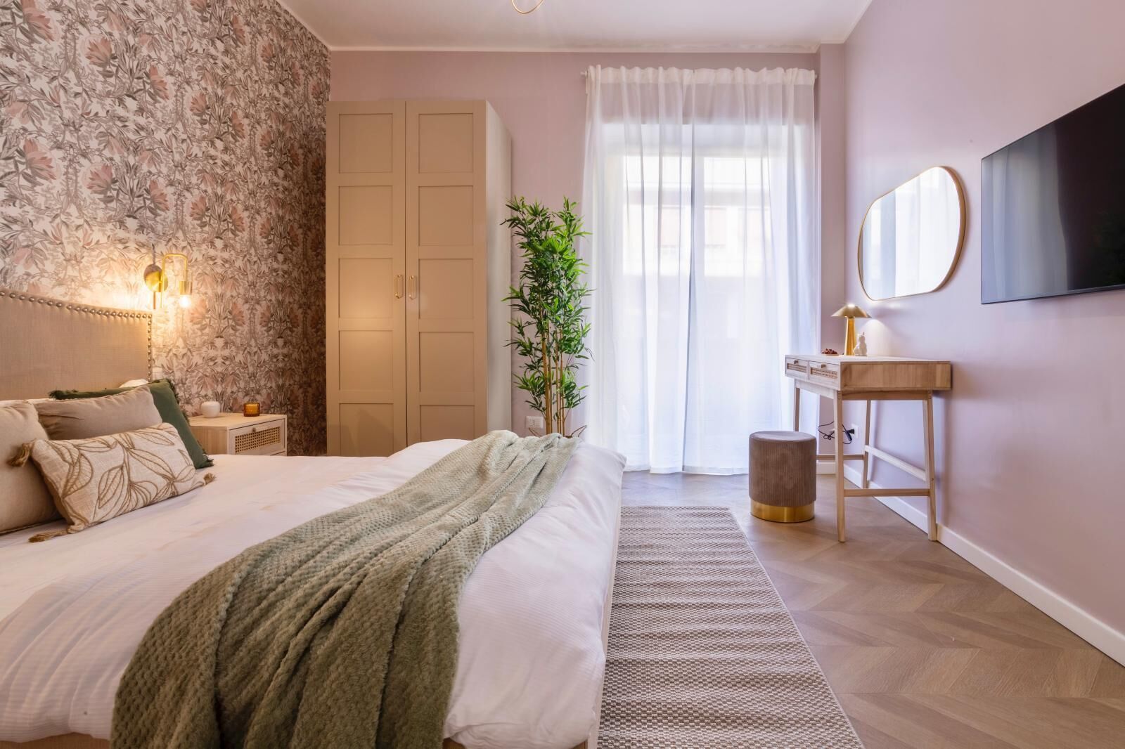 Ein Schlafzimmer mit Bett, Nachttisch, Lampe, Spiegel, Kleiderschrank und einer Topfpflanze.