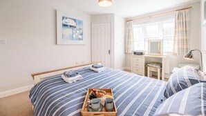 Un dormitorio ordenado con cama, mesitas de noche, un escritorio y una ventana con cortinas.
