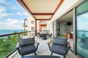 A balcony with two chairs, a table, and a view of the ocean.
