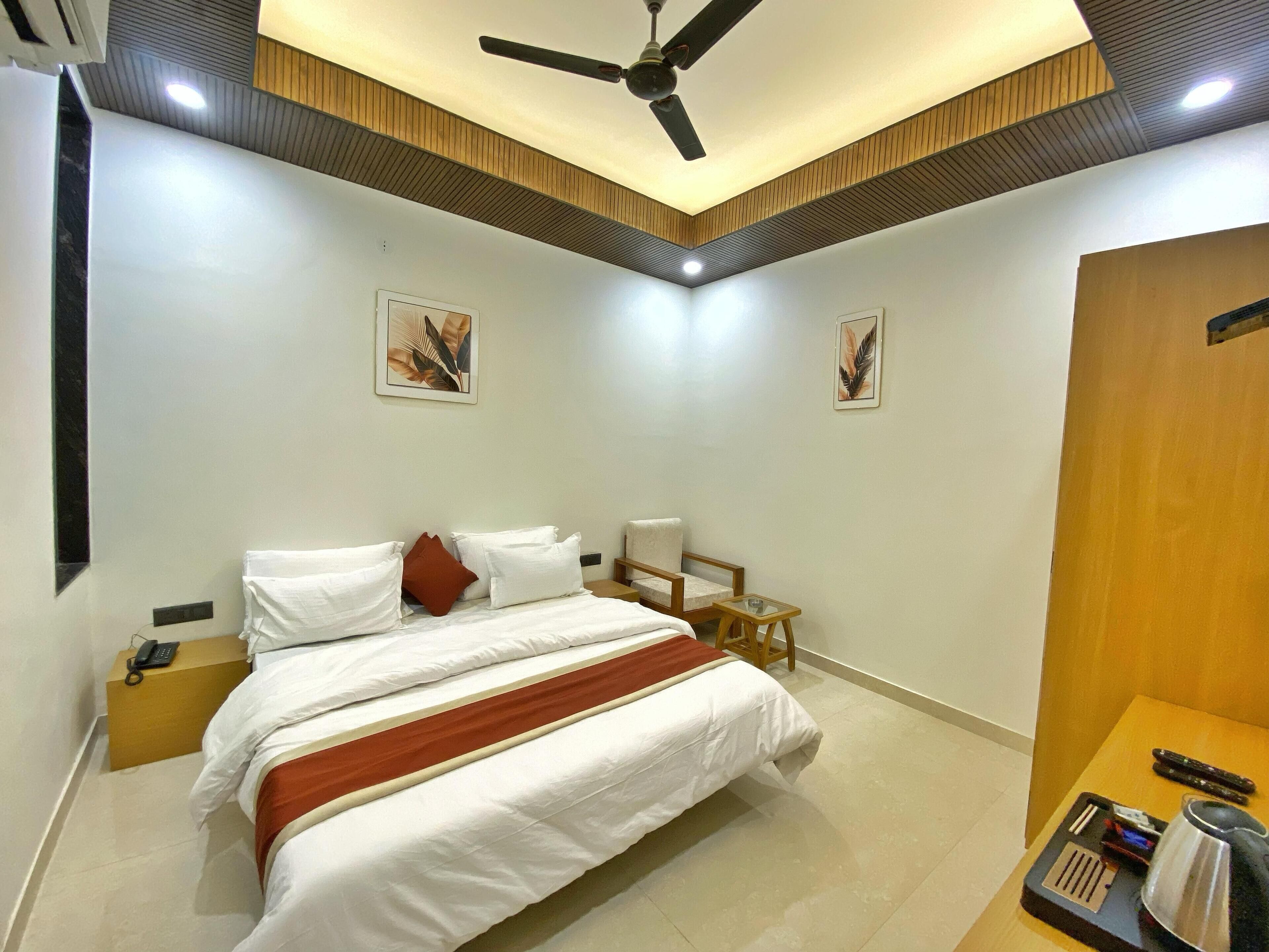 A hotel room with a bed, a chair, a small table, a ceiling fan, and artwork on the walls.
