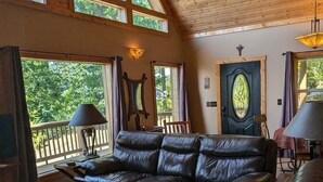 A cozy living room with a leather sofa, a wooden coffee table, and large windows offering a view of the outdoors.
