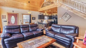 A spacious living room with two leather sofas, a coffee table, and a wooden staircase leading to an upper level.